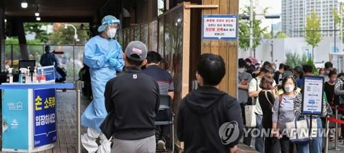 A medical worker watches people standing in line to receive coronavirus tests at a screening clinic in Seoul's Songpa Ward on Sept. 27, 2021. (Yonhap)