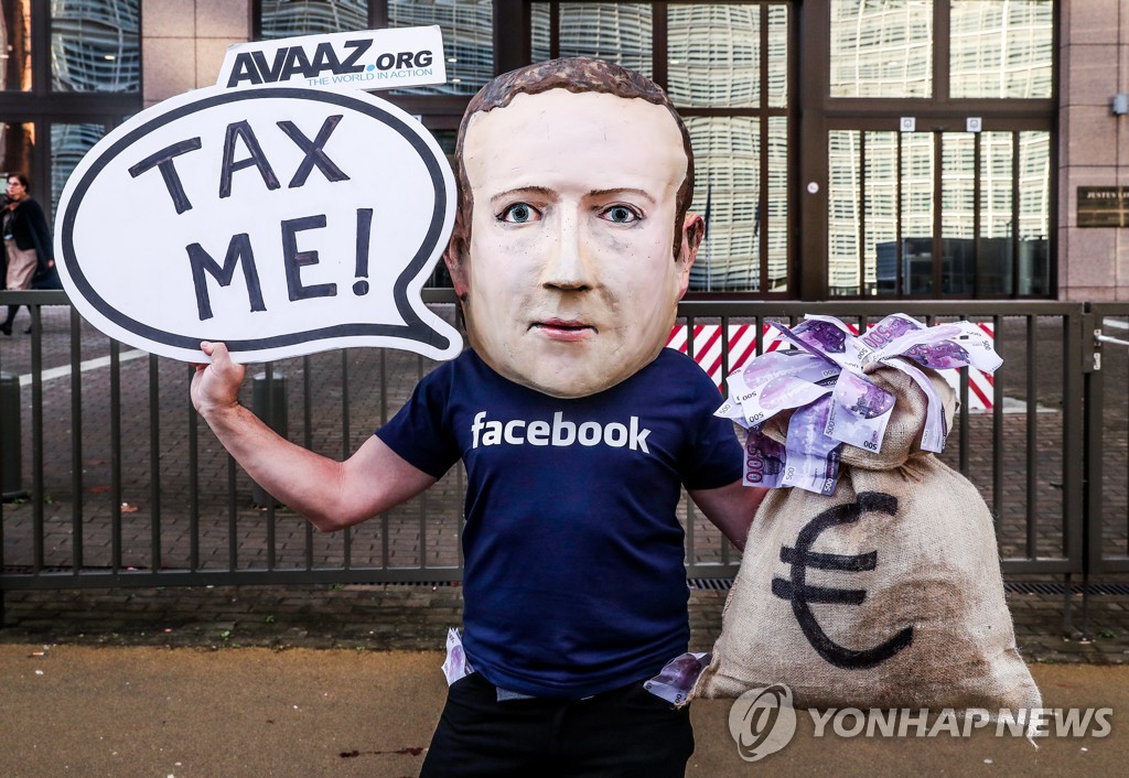 디지털세 도입에 찬성하는 한 시민이 2018년 12월 페이스북 창업자 마크 저커버그의 가면을 쓰고 "세금을 부과해달라"는 피켓을 들고 있다.[EPA=연합뉴스 자료사진]