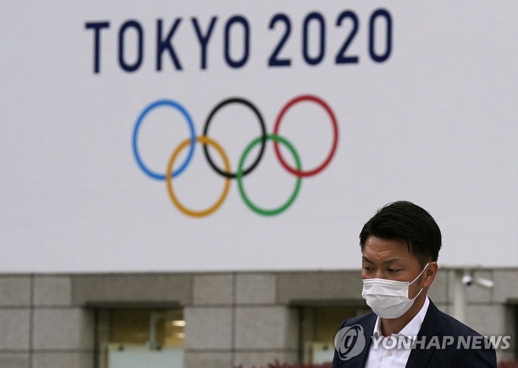 지난달 14일 일본 도쿄에서 한 시민이 시청 건물에 걸린 도쿄올림픽 광고판을 지나치고 있다.