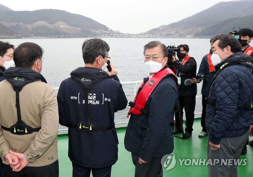 President Moon Jae-in (2nd from R), aboard a ship, listens to acting Busan Mayor Lee Byung-jin (2nd from L) as he views the construction site of an airport on Gadeok Island off the southeastern port city of Busan on Feb. 25, 2021. (Yonhap)
