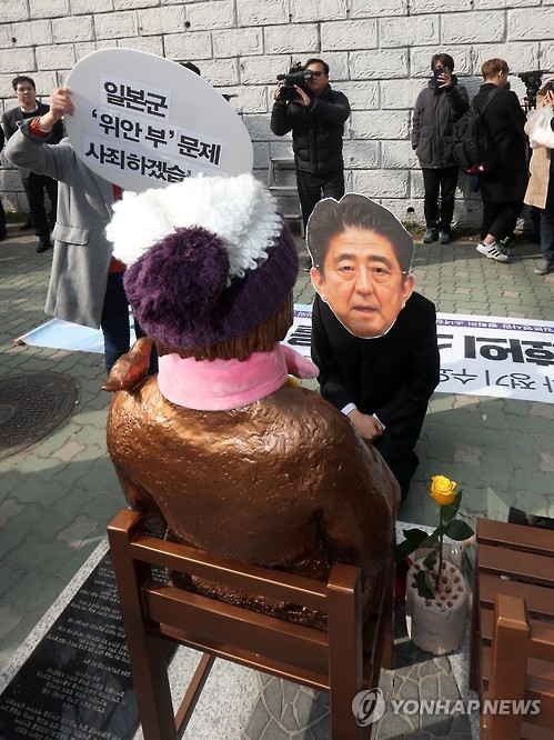A man wearing a mask of Japanese Prime Minister Shinzo Abe's face kneels down in front of the statue of a girl symbolizing the victims of Japan's wartime sexual slavery in front of the Japanese Consulate in South Korea's largest port city of Busan on Jan. 4, 2017, as a civic group holds a rally to support former "comfort women." (Yonhap)