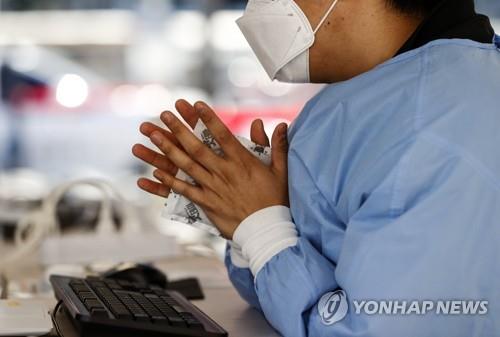 A medical worker warms her hands with an instant hot pack at a makeshift COVID-19 testing station in Seoul on Oct. 17, 2021, amid a cold wave throughout the country. (Yonhap)