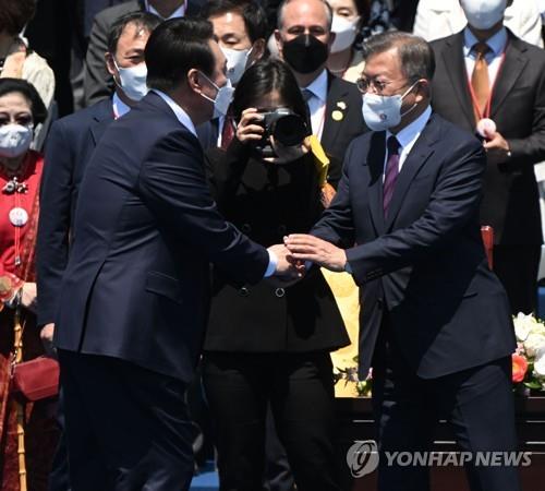 就任式で握手を交わす尹大統領（左）と文前大統領（国会写真記者団）＝１０日、ソウル（聯合ニュース）