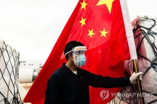 마스크를 쓴 남성이 시노팜 백신 하역을 보며 중국 오성홍기를 들고 있다.