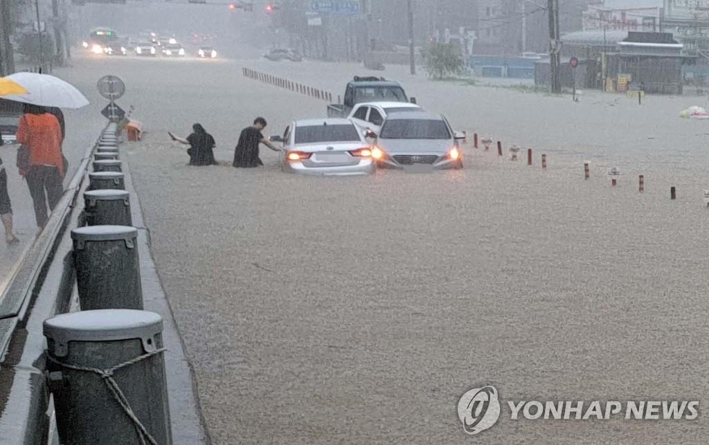 Las personas dejan sus vehículos, el 3 de agosto de 2020, después de que las fuertes lluvias inundaran áreas de Cheonan, provincia de Chungcheong del Sur.