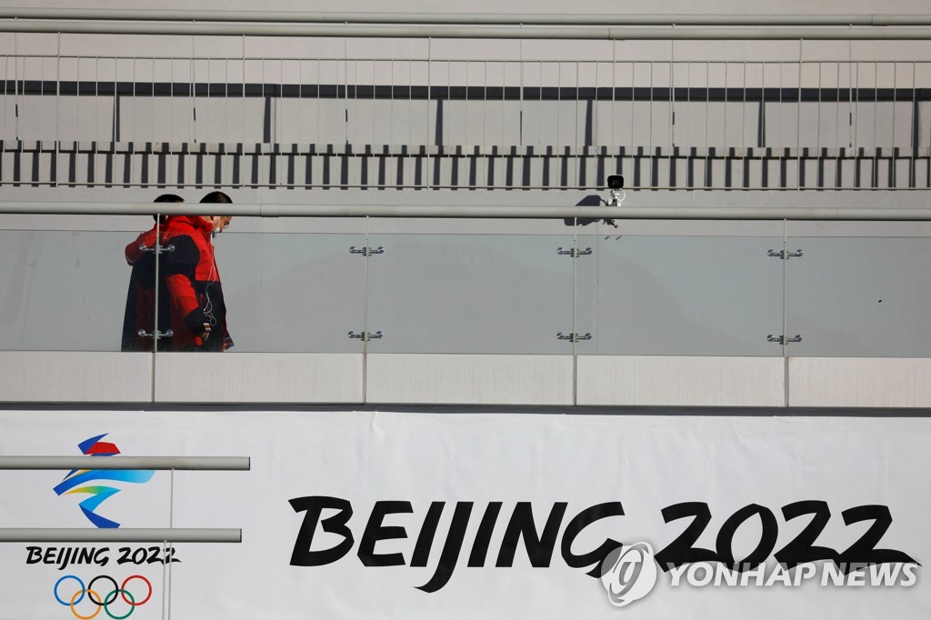 In this Reuters file photo from Dec. 21, 2021, staff members walk by a Beijing 2022 sign at the National Ski Jumping Centre during a media tour to the Winter Olympics venues in Zhangjiakou, northwest of Beijing. (Yonhap)