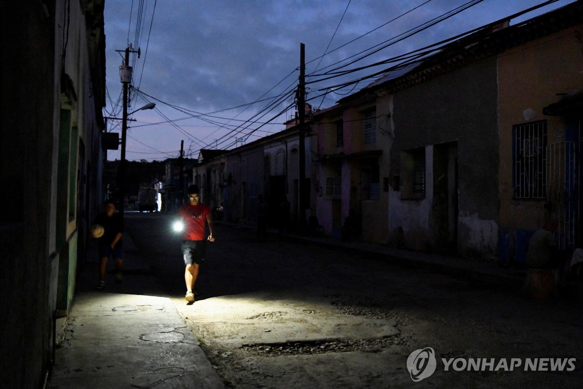 지난 8일(현지시간) 정전된 골목길을 휴대전화 불빛에 의지한 채 지나가는 쿠바 주민