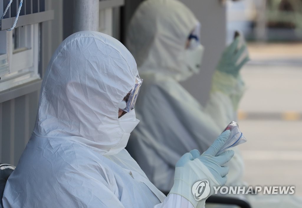 In this file photo taken on March 8, 2020, health workers at a coronavirus drive-through testing center in Daegu look at smartphones during their break time. (Yonhap)