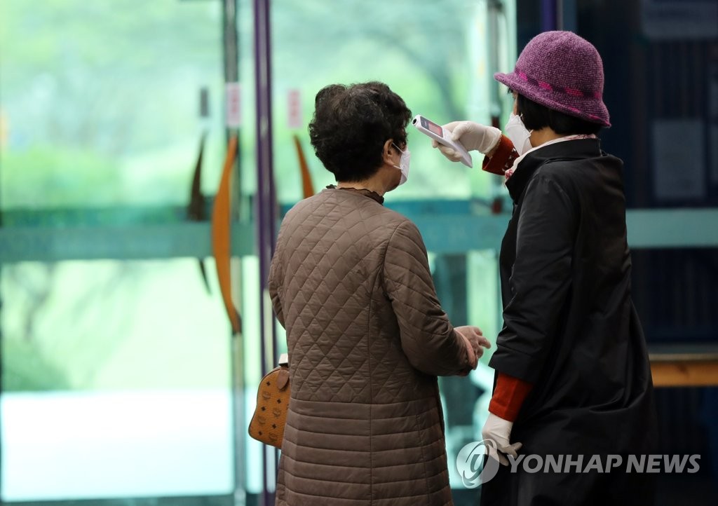 An election official checks the temperature of a voter at a polling station in Gwangju on April 11, 2020. (Yonhap)