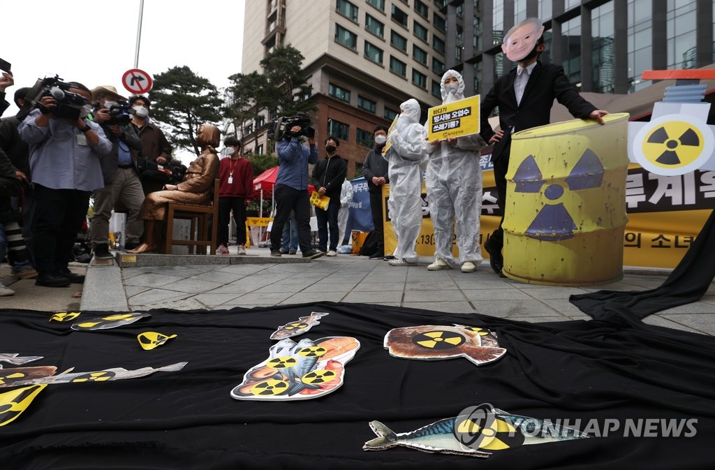 A protestor wearing a mask depicting Japanese Prime Minister Yoshihide Suga simulates the disposal of radioactive water into the ocean during a rally in front of the Japanese Embassy in Seoul on April 13, 2021, as environmental activists express their objection to the Japanese government's decision to discharge water containing radioactive materials stored at the Fukushima nuclear power plant in Japan. (Yonhap)