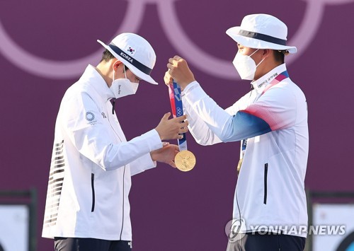 South Korean archer Kim Je-deok (R) puts the gold medal around the neck of his teammate An San during the medal ceremony for the mixed team event at the Tokyo Olympics at Yumenoshima Park Archery Field in Tokyo on July 24, 2021. (Yonhap)