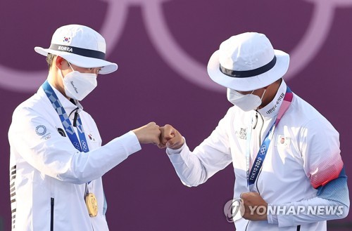 South Korean archers An San (L) and Kim Je-deok bump fists after winning the gold medal in the mixed team event at the Tokyo Olympics at Yumenoshima Park Archery Field in Tokyo on July 24, 2021. (Yonhap)
