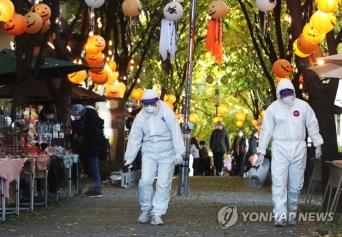 Health workers spray disinfectant along the avenue of a popular hangout in Yongin, Gyeonggi Province, ahead of Halloween festivities, on Oct. 27, 2021. (Yonhap) 