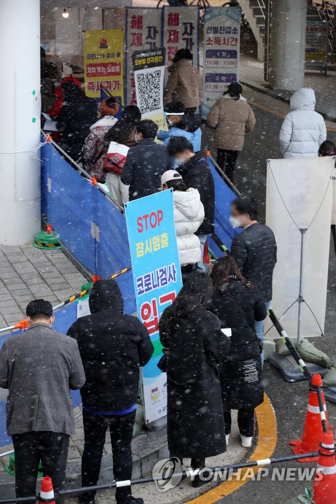 People in thick winter clothes wait in line for coronavirus tests at a pop-up screening clinic in the southwestern city of Gwangju on Dec. 17, 2021, as snow falls, with the mercury dipping to a low of 1 C. South Korea's new coronavirus cases stayed above 7,400 for the third consecutive day, with the country set to restore tight social distancing and other virus curbs to contain the fast spread of the virus. (Yonhap)