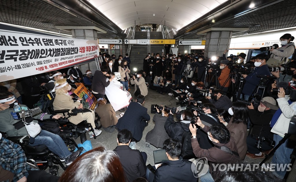 Activists, citizens and journalists watch as a wheelchair-bound female protester has her head shaved in a rally by the Solidarity Against Disability Discrimination (SADD) on March 30, 2022, at the Gyeongbokgung subway station in central Seoul. (Yonhap)