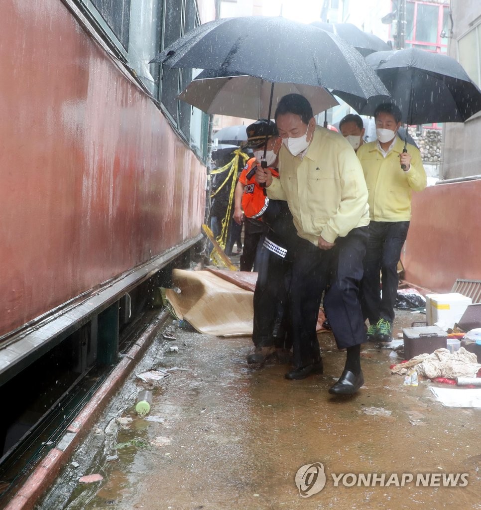 Le président Yoon Suk-yeol (au c.) inspecte un logement en demi-sous-sol dans l'arrondissement de Gwanak à Séoul, le mardi 9 août 2022, où trois membres d'une famille ont été retrouvés morts après des pluies diluviennes qui ont frappé Séoul et les parties centrales du pays la veille.