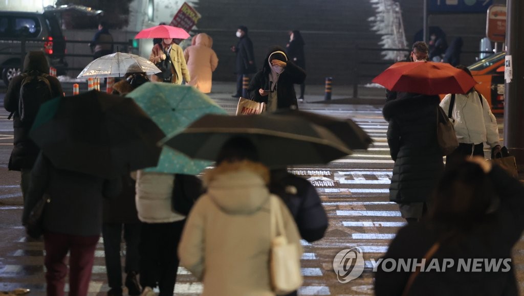 前日はソウルをはじめとする首都圏で朝から雪が降り、午後は雨に変わった。傘を差しながらソウル駅前を歩く市民＝２１日、ソウル（聯合ニュース）