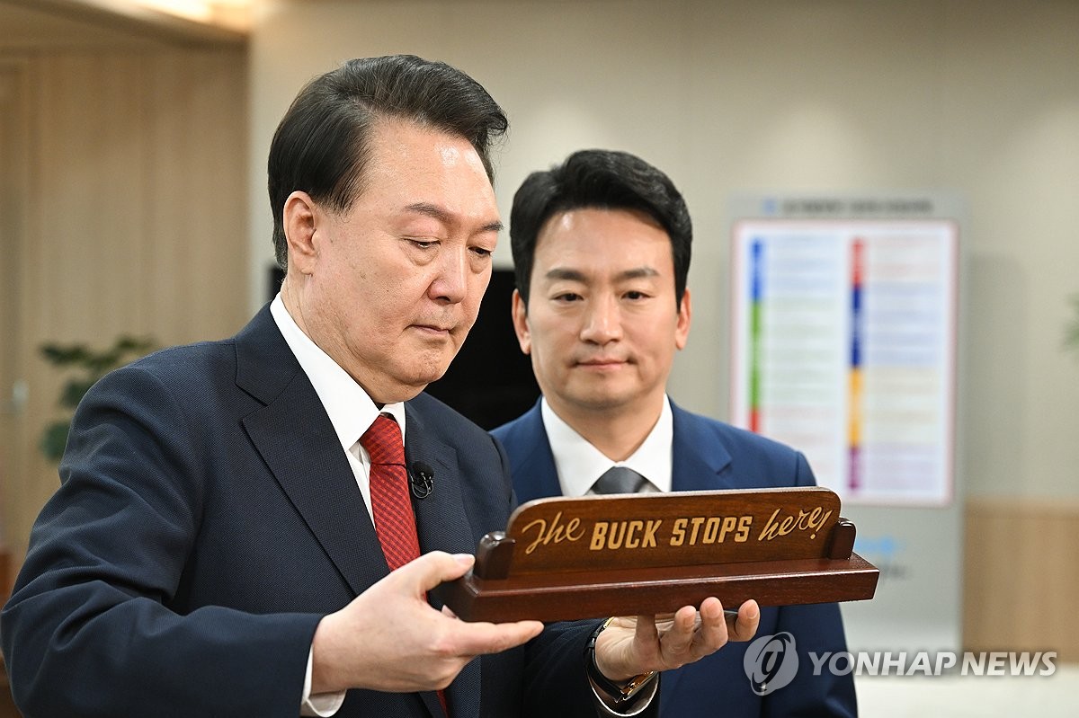 El presidente Yoon Suk Yeol (izq.) presenta una réplica del libro de Truman. "El dinero se detiene aquí" placa de escritorio, regalada por el presidente estadounidense Joe Biden durante las conversaciones cumbre en Seúl en mayo de 2023, a un presentador de KBS después de grabar una entrevista especial con la emisora ​​estatal en la oficina presidencial en Seúl el 4 de febrero de 2024, en esta foto proporcionada por la oficina.  (FOTO NO EN VENTA) (Yonhap)